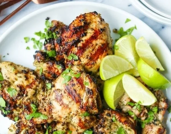 Cilantro lime chicken thighs on a plate with fresh herbs and lime wedges